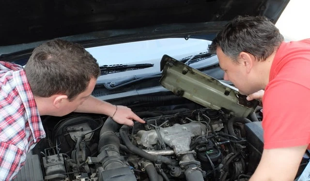 Мужчина показывает пальцем на деталь под капотом